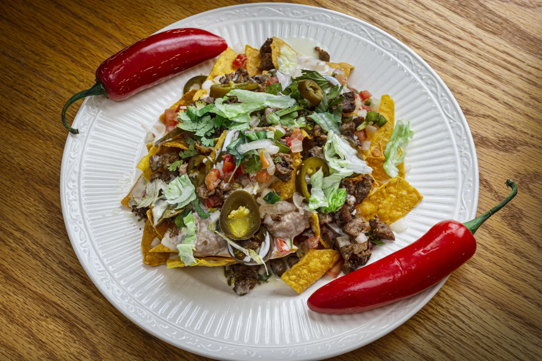 Nachos on a white plate with jalapenos